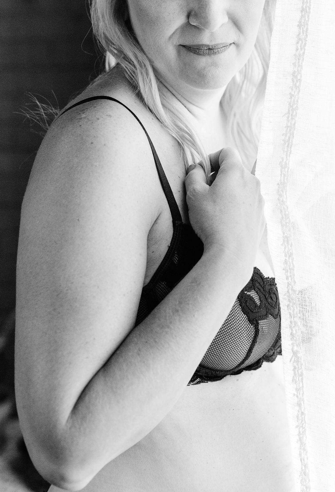 black and white boudoir photo by self love photo co woman in lingerie peeking out from curtain