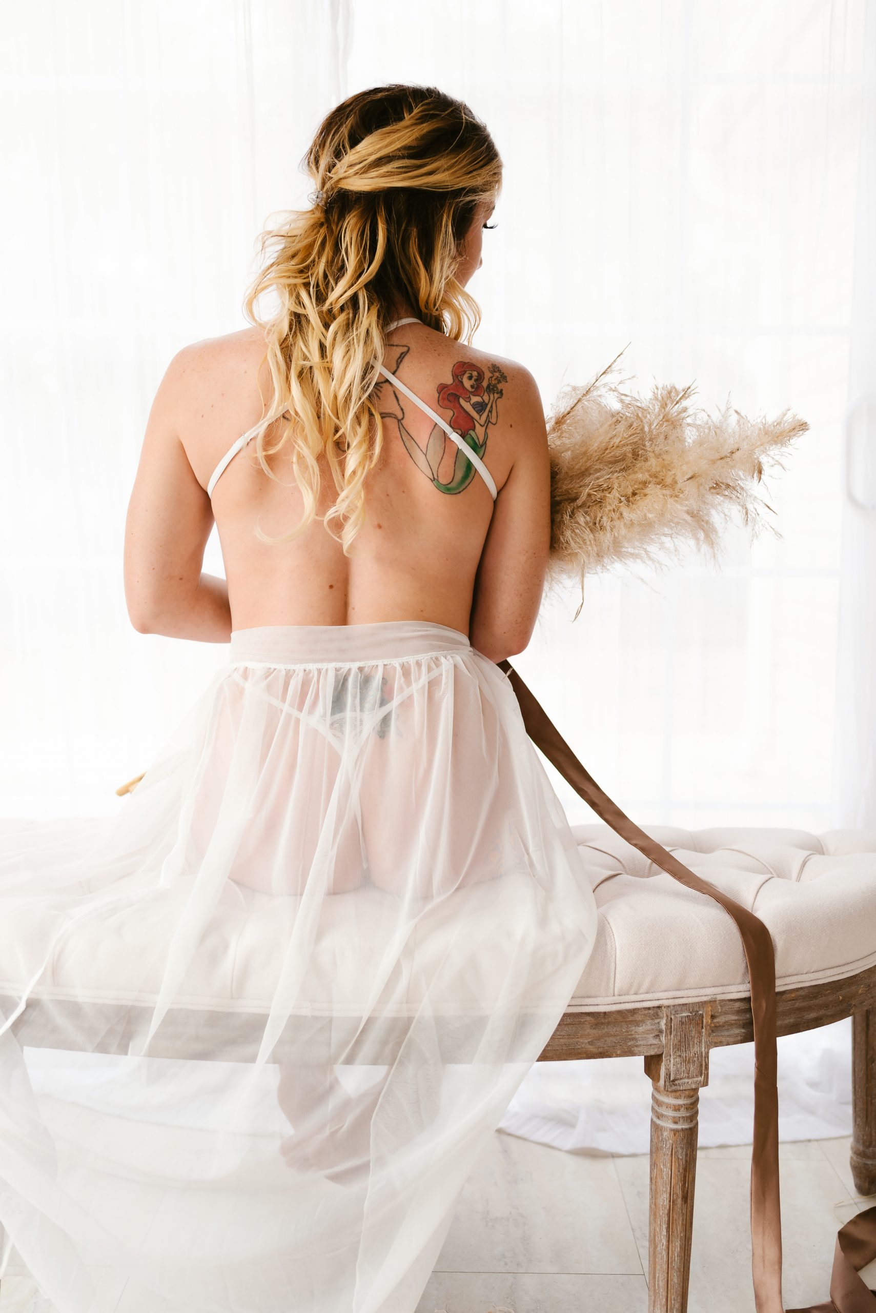 woman sitting on bench with pampas grass posing for boudoir photo